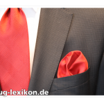 Rotes, unifarbenes Einstecktuch in Rosettenfaltung bei einem karierten Business-Anzug mit passender Krawatte